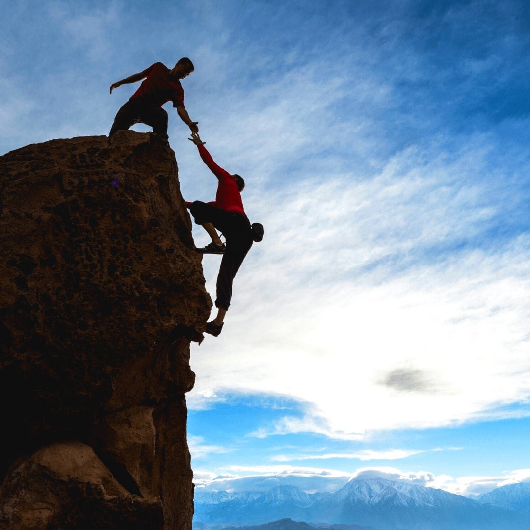a photo of a man on top of a cliff reaching down to help his climbing partner reach the top. music mentor